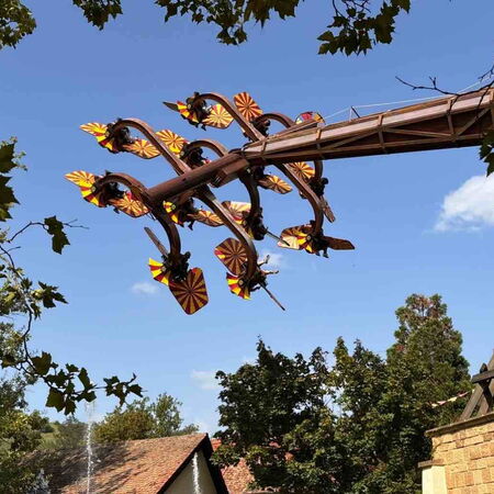 Eine aufregende Achterbahn mit Schmetterlingsdekorationen fliegt unter einem strahlend blauen Himmel durch die Luft.