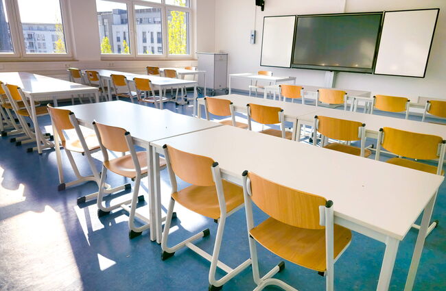 Ein heller Unterrichtsraum mit mehreren Tischen und Stühlen, bereit für Schüler und Lehrer.