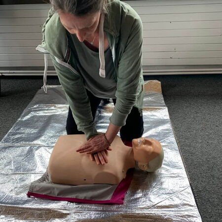 Eine Frau übt Erste-Hilfe-Maßnahmen an einer Puppe auf einer Rettungsdecke während eines PädTag-Workshops.