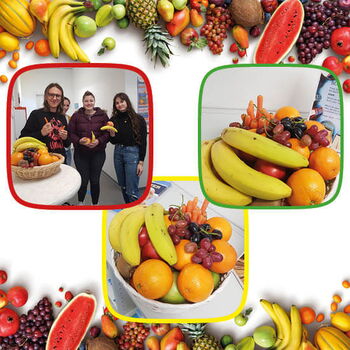 Drei Personen präsentieren einen Obstkorb mit Bananen, Orangen und Trauben bei einem Infoabend.