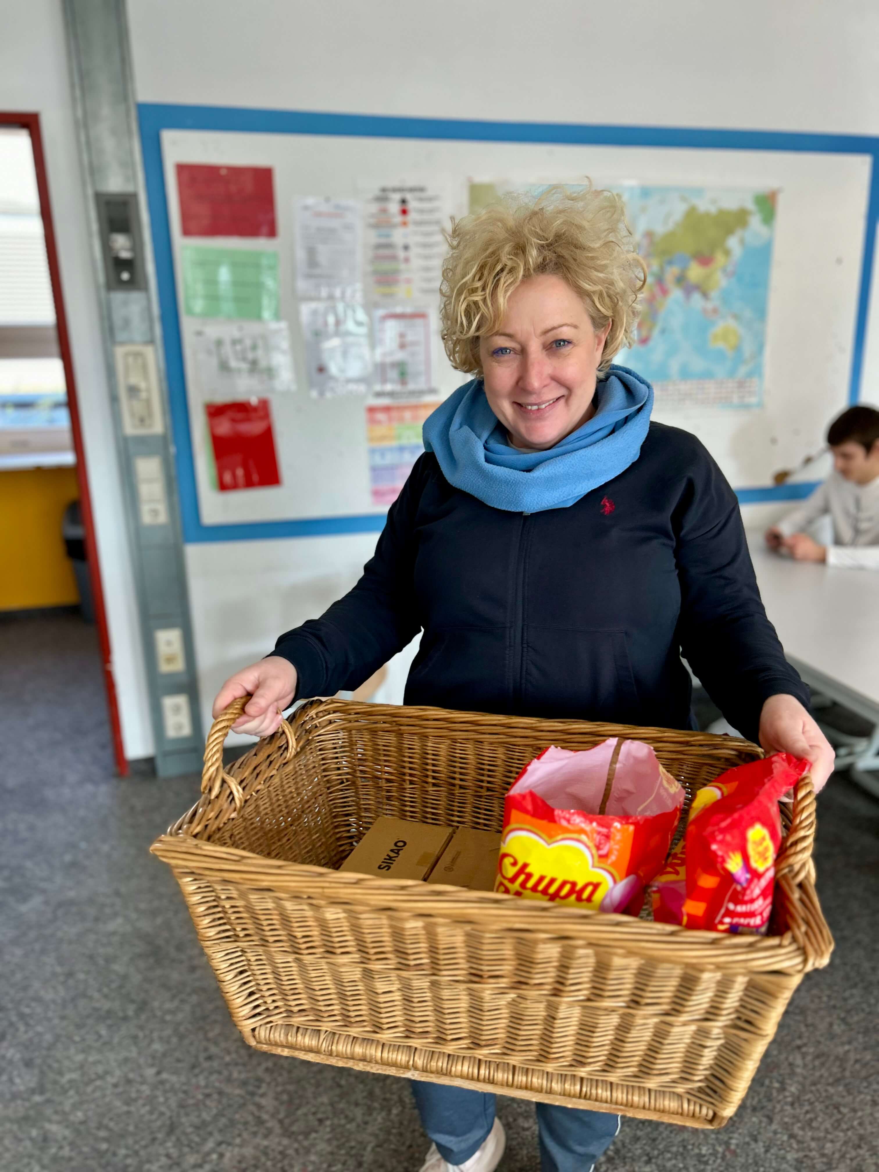 Eine lächelnde Frau trägt einen Korb voller Geschenke zum Zuckerfest in einem Klassenraum.