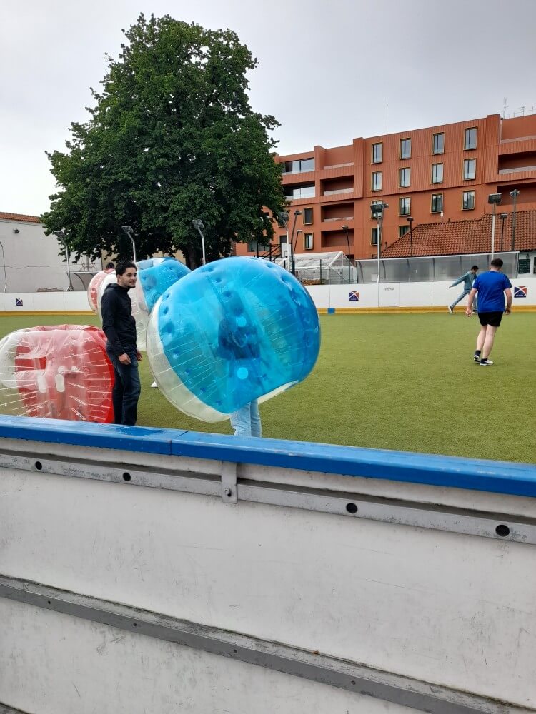 Zwei Menschen stehen mit aufblasbaren Ballons auf einem Sportplatz, während andere spielen.