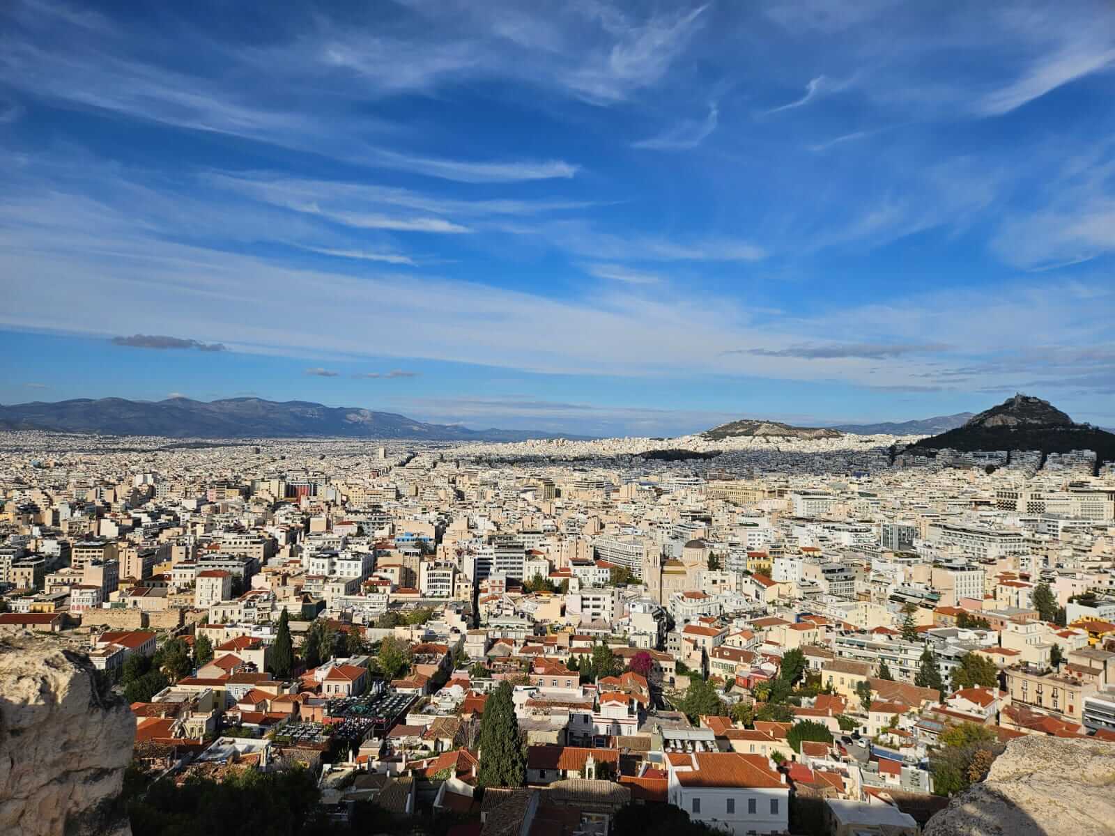 Weitblick über Athen, mit blauem Himmel und Hügeln im Hintergrund, zeigt die urbane Ausdehnung der Stadt im November 2025.